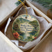 A circular ornament with a tropical landscape design, featuring a river, palm trees, and a bridge, is displayed in a box.