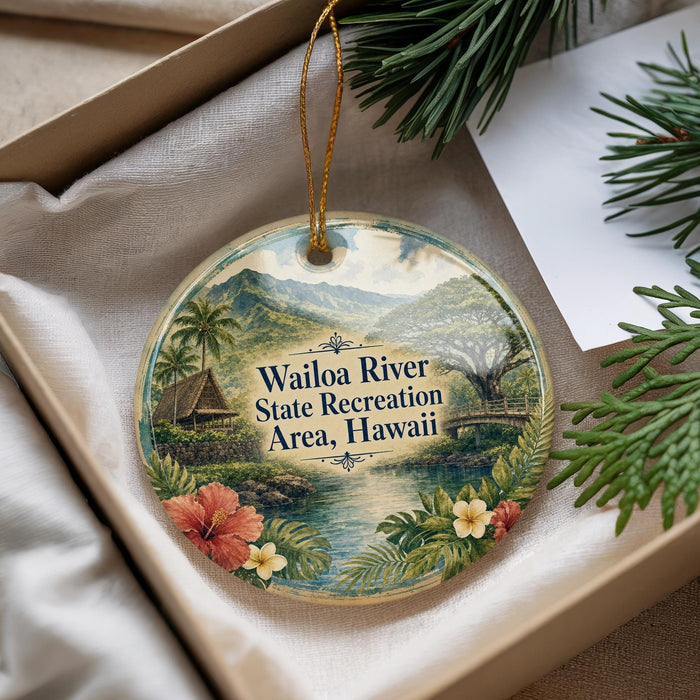 A decorative ornament with a tropical landscape, featuring a river, palm trees, and flowers, is displayed in a box with pine branches.