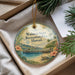 A decorative ornament with a tropical island scene, featuring a pier, palm trees, and a beach, is displayed in a box with pine branches.