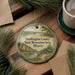 A decorative ornament with a scenic landscape of Washington County, Illinois, featuring a lake, mountains, and a gazebo, is displayed on a wooden surface alongside a cup of coffee and some pine branches.