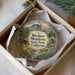 A round ornament with a scenic landscape of mountains, trees, and a cabin, hanging from a string.