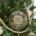 A round ornament hanging on a Christmas tree, featuring a scenic landscape with mountains, a cabin, and a deer.