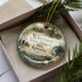 A decorative ornament in a box, featuring a scenic image of the state historic site in Kentucky.