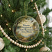 A round ornament hanging on a Christmas tree, featuring a scenic landscape with a deer and a bird in flight.