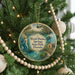 A round ornament hanging on a Christmas tree, featuring a mermaid and a house surrounded by palm trees.