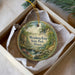 A decorative ornament in a white box, featuring a scenic landscape with a waterfall and a house, with the text "Weinberg-King State Park, Illinois" printed on it.