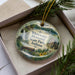 A decorative ornament in a box, featuring a scenic landscape with a waterfall, a bench, and a building, along with the text "Whewater Memorial State Park, Indiana".