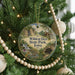 A round ornament hanging on a Christmas tree, featuring a scenic landscape with a waterfall and a cabin in the background.