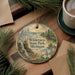 A decorative ornament featuring a scenic landscape with a waterfall, pine trees, and a deer, placed on a wooden surface alongside a cup of coffee and some papers.