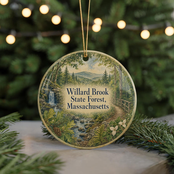 A round ornament with a painting of a forest scene hangs in front of a Christmas tree with lights.