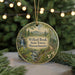 A round ornament with a painting of a forest scene hangs in front of a Christmas tree with lights.