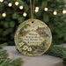A round ornament with a painting of a historic house and a wreath, surrounded by greenery and white flowers, with the text "William Whitley House State Historic Site, Kentucky" displayed on it.