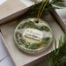 A decorative ornament in a box, featuring a scenic landscape of Willowdale State Forest in Massachusetts.