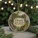 A round ornament with a scenic forest landscape and text, hanging from a string.