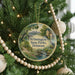 A round ornament hanging on a Christmas tree, featuring a scenic landscape with a waterfall and a bridge.