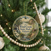 A round ornament hanging on a Christmas tree, featuring a scenic landscape with a waterfall and a cabin in the background.