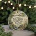 A round ornament with a painting of a wolf and a cabin, surrounded by greenery, hangs in front of a blurred background with twinkling lights.