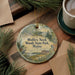 A decorative ornament with a scenic image of Wolf's Neck Woods State Park, Maine, is displayed on a wooden surface alongside a cup of coffee and some pine branches.