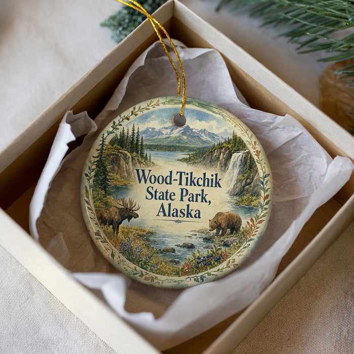 A decorative ornament in a box, featuring a scenic landscape with moose and a mountain backdrop, with the text "Wood-Tikchik State Park, Alaska" prominently displayed.