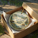 A round ornament in a wooden box, featuring a scenic landscape with a moose and bear, and the text "Wood-Tikchik State Park, Alaska".
