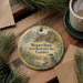A decorative ornament with a bird perched on a rock, surrounded by pine branches and a cup of coffee on a wooden surface.