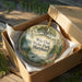 A decorative ornament in a brown box, featuring a scenic landscape with a tree, lake, and wildlife.
