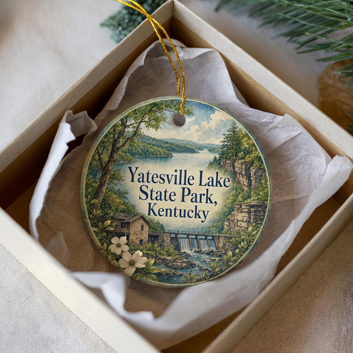 A decorative ornament in a box, featuring a scenic landscape with a lake, trees, and a waterfall.