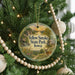 A round ornament hanging on a Christmas tree, featuring a scenic landscape with a deer and a path leading to a cabin.