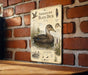 a metal sign with illustrations and text about the American Black Duck, mounted on a brick wall.