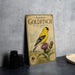 A vintage-style metal sign featuring an illustration of a goldfinch on a thistle plant, with text describing the bird species.