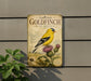 a vintage-style sign with an illustration of a goldfinch perched on a thistle, mounted on a wall.
