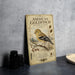 A vintage-style metal plaque featuring an illustration of an American Goldfinch, with text describing the bird and its habitat.