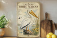 a large illustration of a white pelican standing on a log, surrounded by flowers and plants, with a wooden paddle and a potted plant nearby.