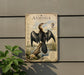 a metal plaque with an illustration of a bird, specifically an Anhinga, perched on a log. The Anhinga is depicted in a detailed and realistic manner, showcasing its unique features and characteristics. The plaque is mounted on a wall, and there is a plant visible in the foreground, adding a touch of nature to the scene.