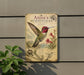 a vintage-style metal sign with illustrations and text about a hummingbird, mounted on a wall next to a plant.