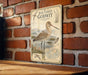 a vintage-style metal sign with a detailed illustration of a bar-tailed godwit, a type of wading bird, mounted on a brick wall.