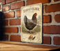 A vintage-style metal sign featuring an illustration of a chicken, mounted on a brick wall.