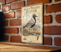 A vintage-style metal sign with a black and white illustration of a bird, mounted on a brick wall.