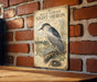 a vintage-style metal sign with a black-crowned night-heron illustration, mounted on a brick wall.