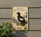 a vintage-style metal plaque with an illustration of a black bird, likely a guillemot, perched on a rock. The plaque is mounted on a wall, and there is a plant to the left of the plaque.