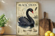 a vintage-style poster of a black swan, with illustrations and text, displayed on a shelf next to a wooden cutting board and some potted plants.