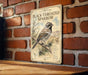 a vintage-style sign with a black-throated sparrow illustration, mounted on a brick wall.