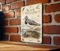 A metal sign with a bird illustration is mounted on a brick wall.
