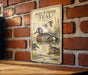 a vintage-style metal sign with illustrations of blue-winged teal ducks, mounted on a brick wall.