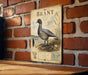 A vintage-style metal sign with an illustration of a bird, likely a duck, mounted on a brick wall.