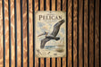 A vintage-style poster of a pelican in flight, mounted on a wooden wall.