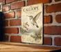 A vintage-style metal sign with a detailed illustration of a hummingbird, mounted on a brick wall.