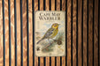 a vintage-style poster of a bird, specifically the Cape May Warbler, displayed on a wooden wall.