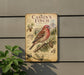 a sign with a detailed illustration of a red bird perched on a branch, surrounded by pine cones and other natural elements.