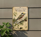 a vintage-style metal sign with a bird illustration, mounted on a wall next to a plant.